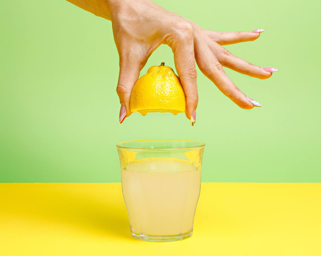 Handpressar en halv citron över ett glas lemonad